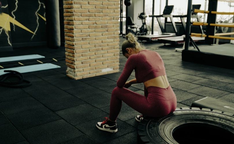 A woman in sportswear rests on a tire during gym training, showcasing fitness dedication.